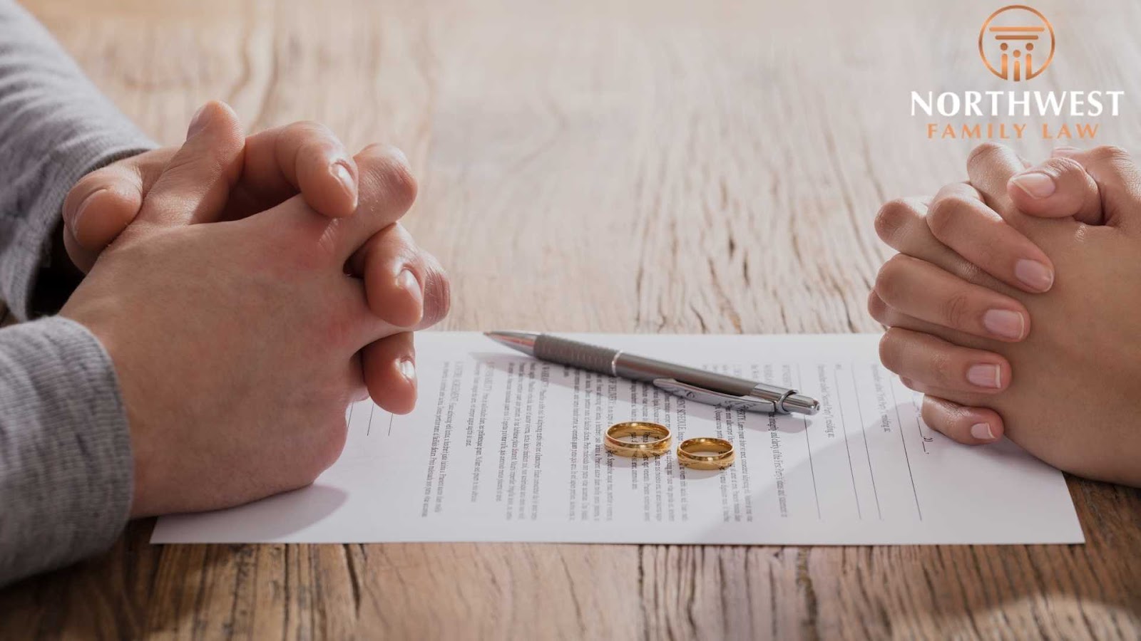 Two hands clasped over divorce papers and rings.