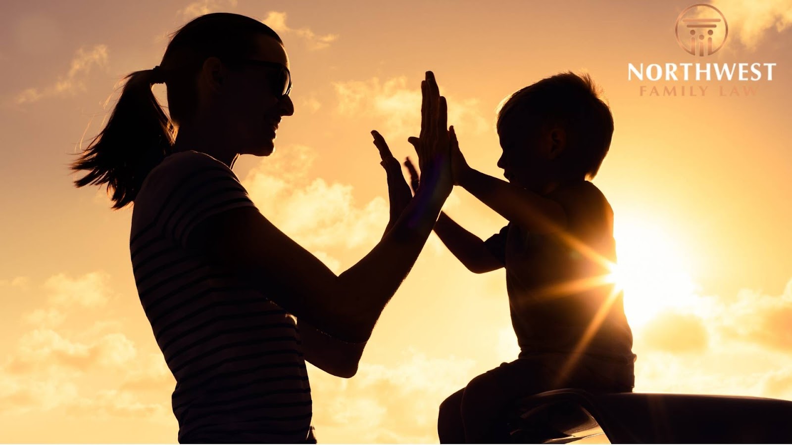 Silhouette of parent and child high-fiving at sunset.